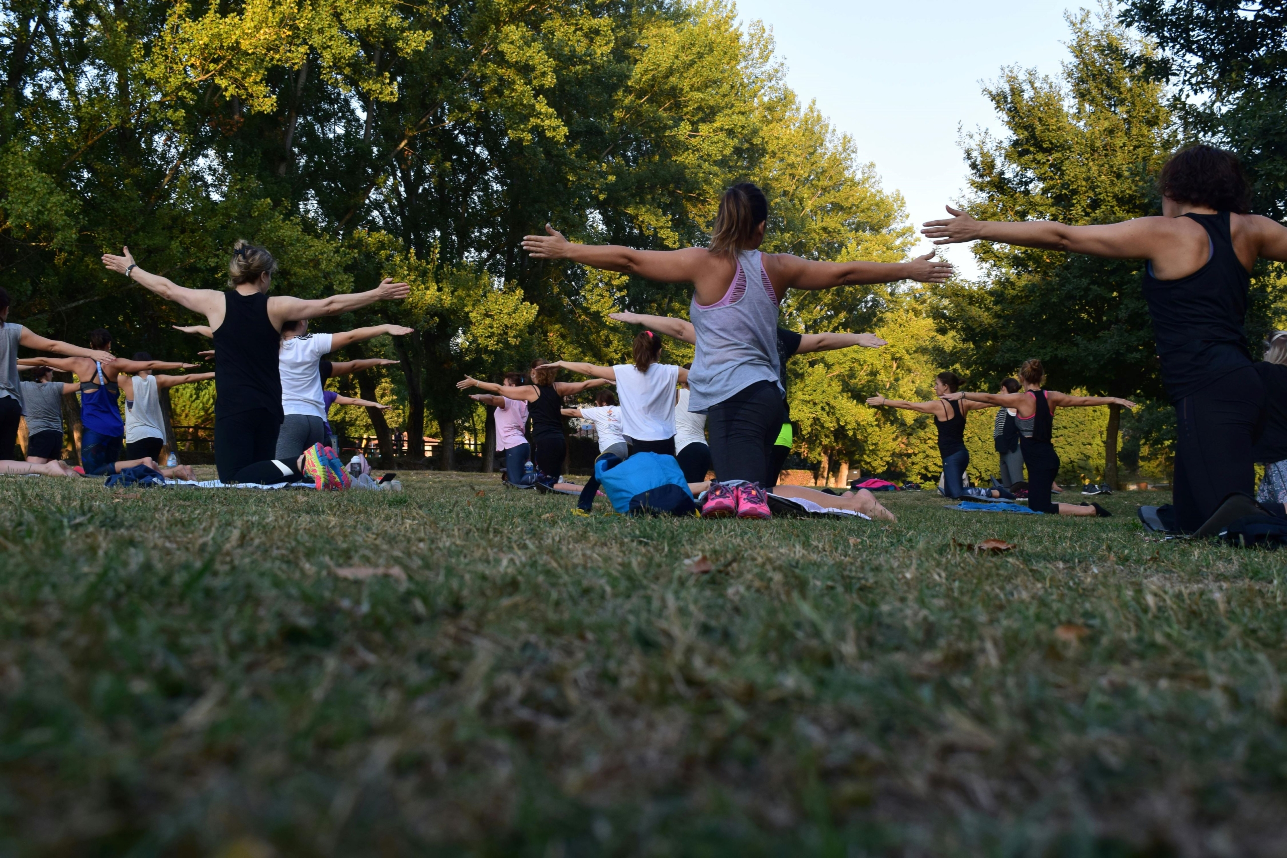 A group of people kneeling and holding their arms out in an outdoor yoga class