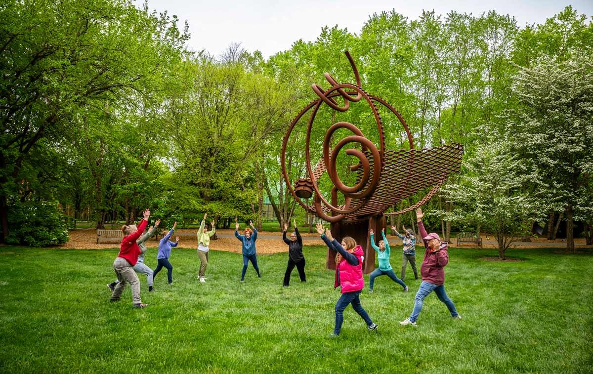 A group of ten people in a semi circle doing Tai Chi outdoors.